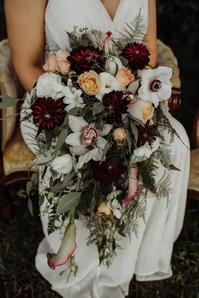 Large bridal bouquet. Wedding florals including white, dark red, orange, and green flowers.