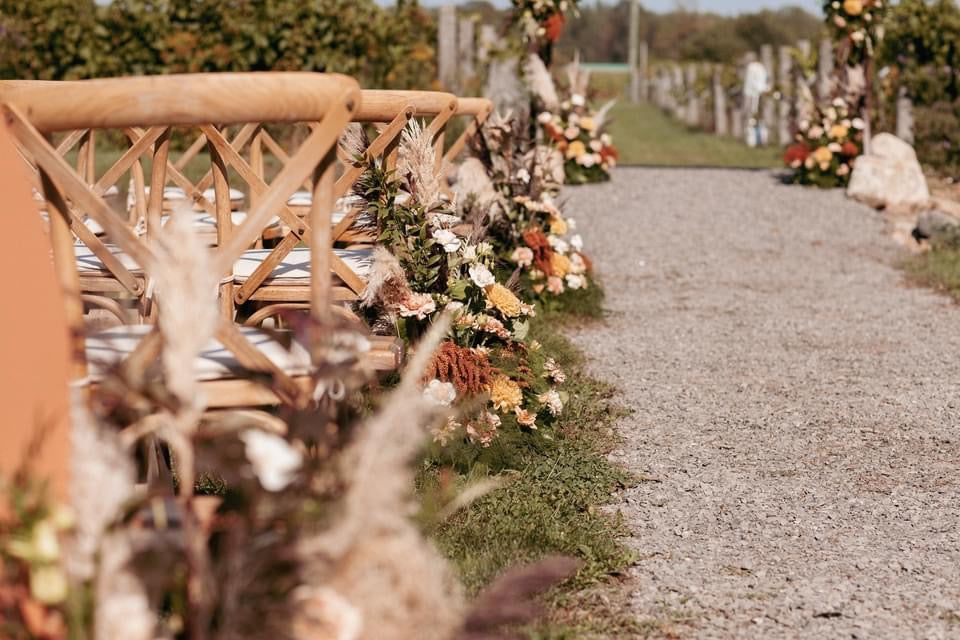 Wedding florals lining the wedding aisle. Orange, yellow, green, and cream colored florals.