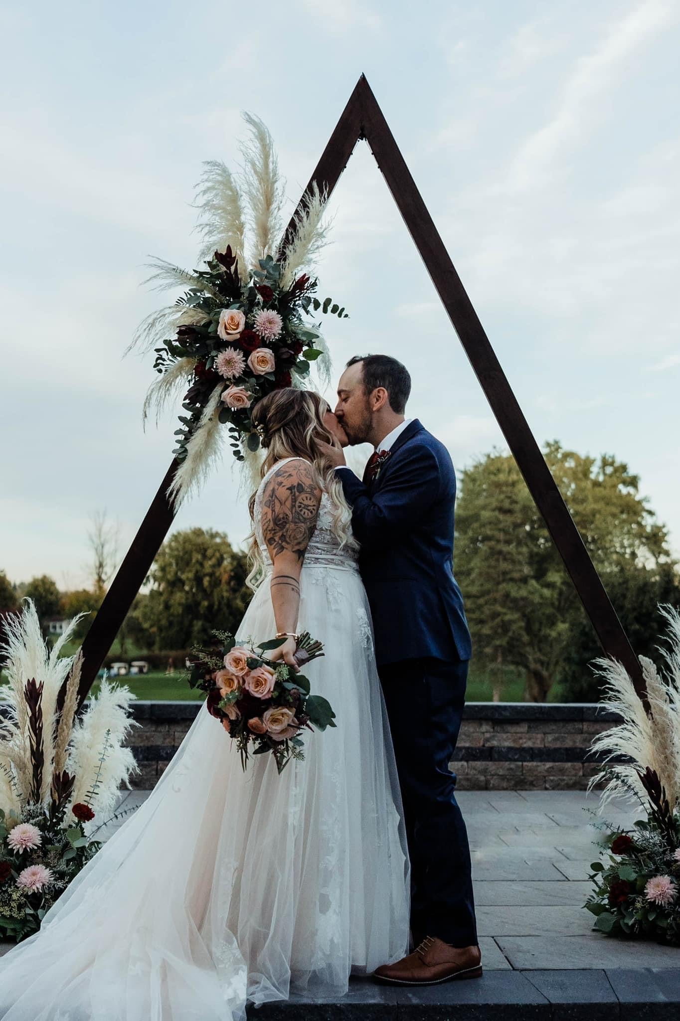 Boho wedding alter florals. Couple kissing at the alter surrounded by boho style florals including pink, green, and cream colored florals.